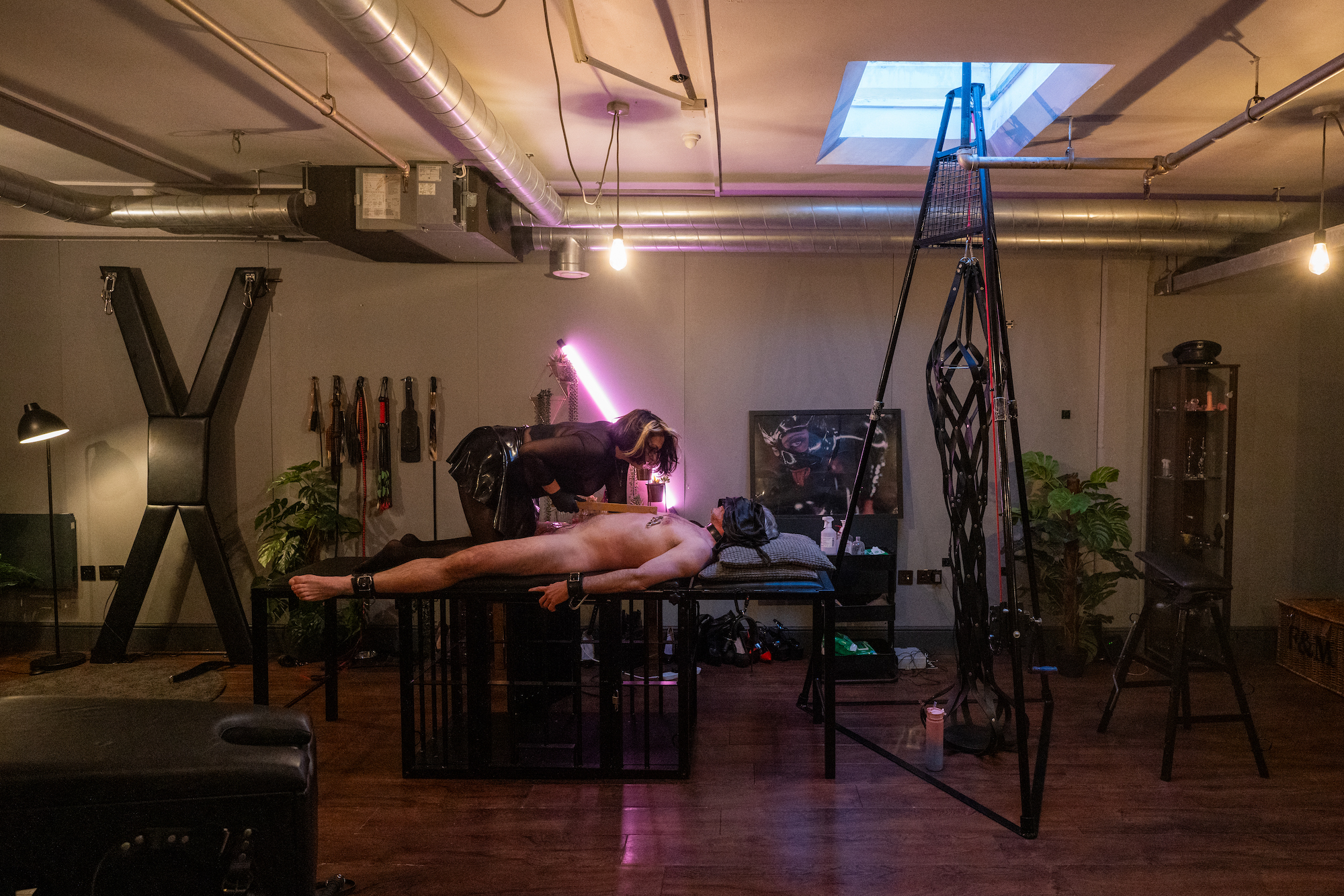 Dominatrix Countess Diamond leaning over a naked male sub in a dungeon