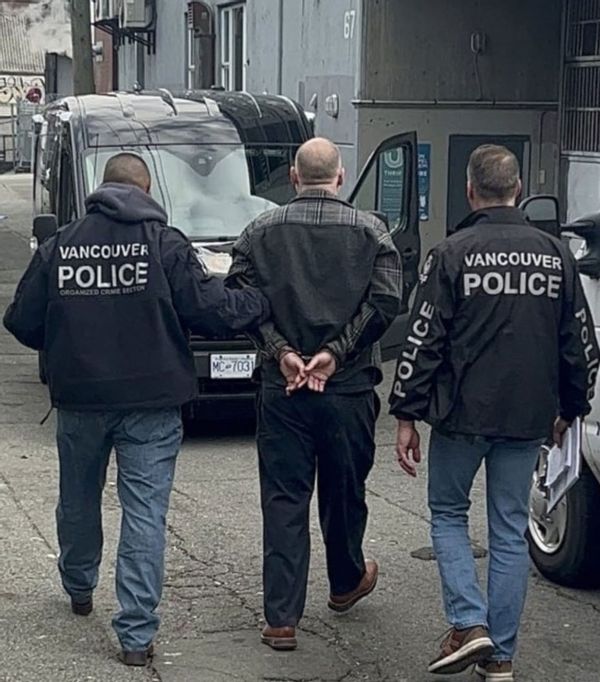 A photo of Larsen being led away by two policemen towards a black van. 
