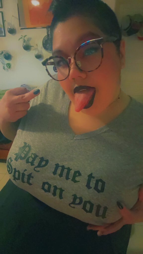 Dominatrix Queen Rini wearing shirt saying "pay me to spit on you"