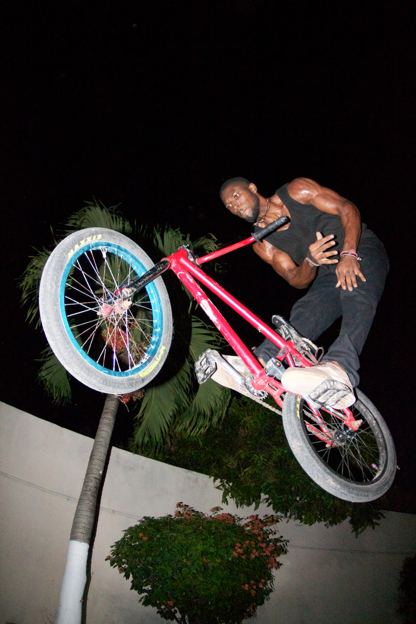 A man in a black vest flies through the air on his BMX bike without holding the handlebars.