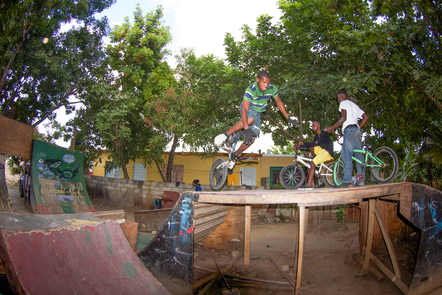 A man rides a black BMX on one front wheel over a wooden ramp.