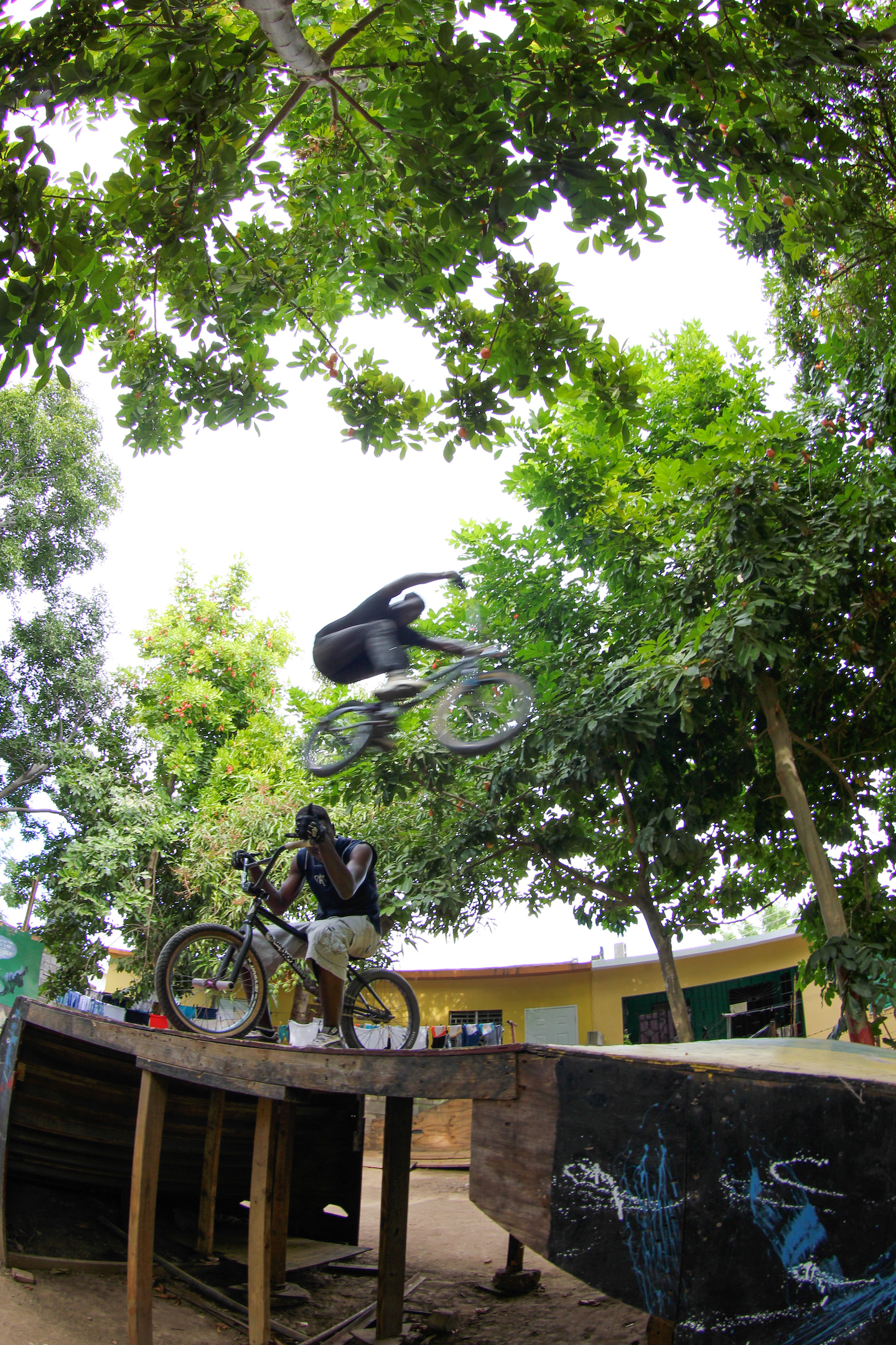 The blurred image of a man on a bike leaping over another man below on a bike.