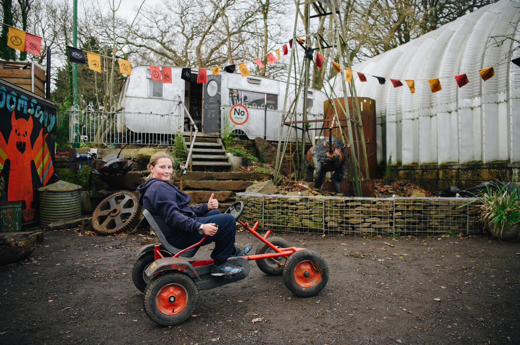 A kid rides a toy vehicle through the yard of a DIY community.