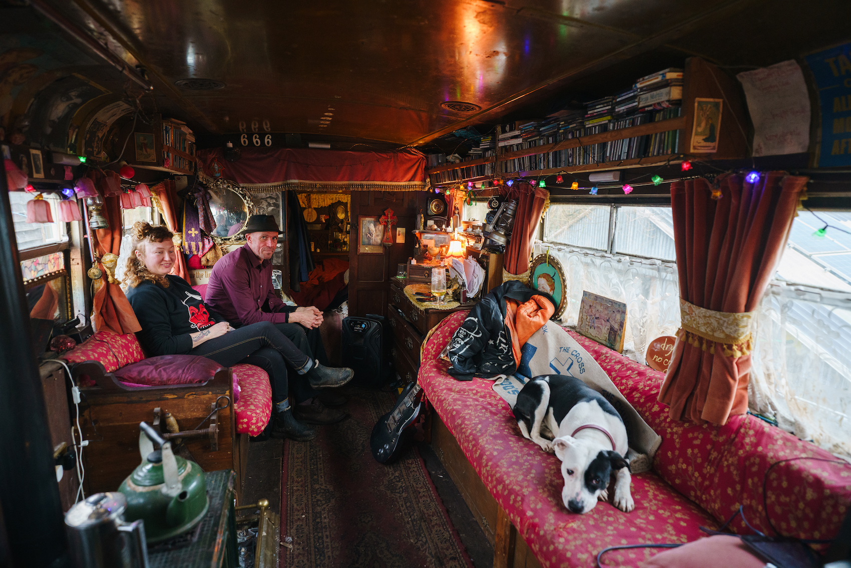 A couple sit in their caravan with their dog, surrounded by red decor.