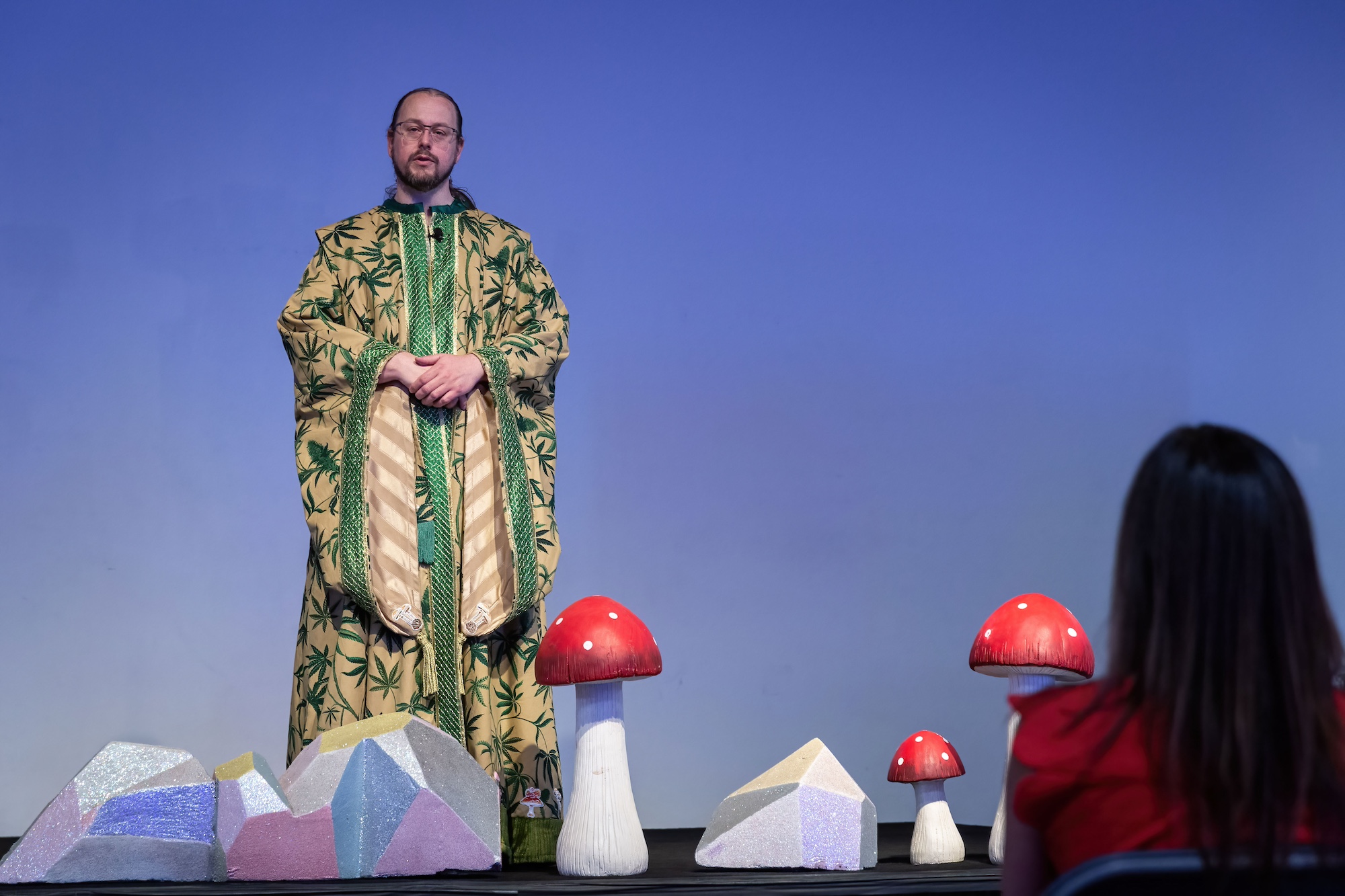 A man in a green and gold robe preaches from a stage