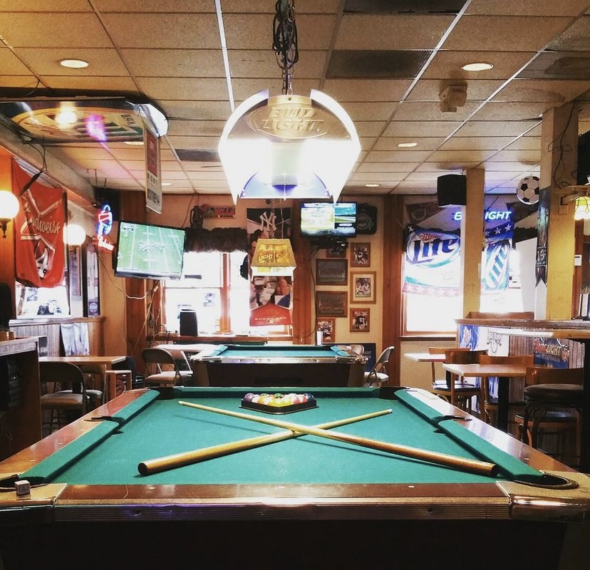 A photo of a bar containing pool tables and a TV screen.