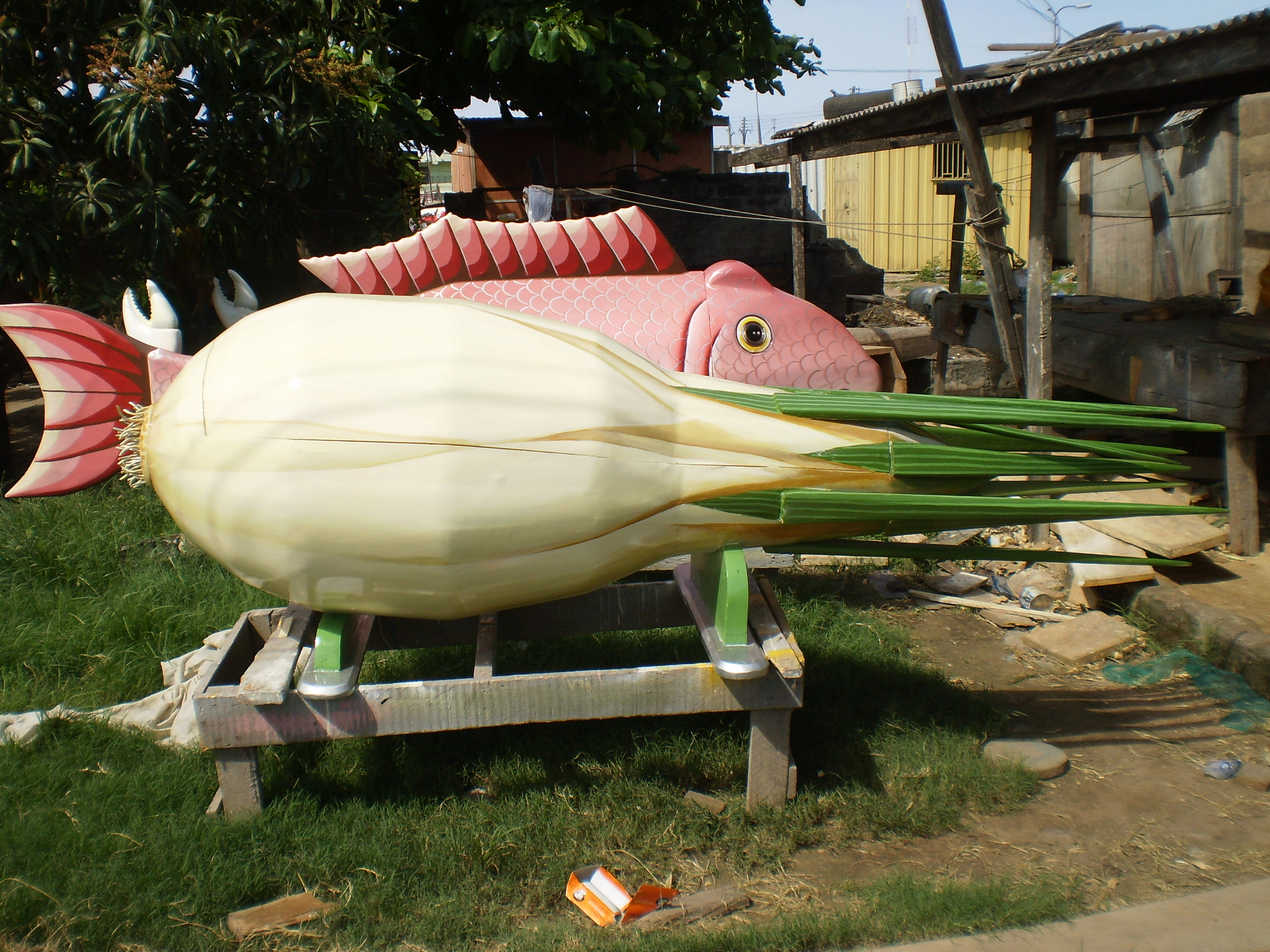 Two novelty coffins in a yard, one fish shaped and one vegetable shaped.