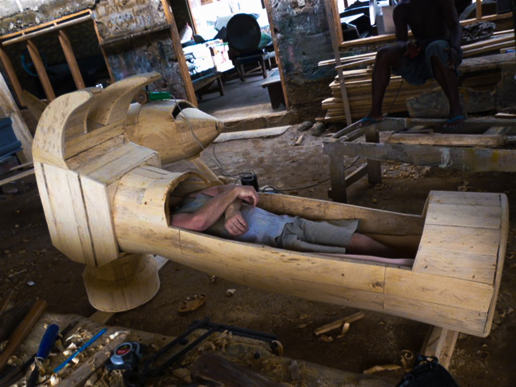 A man lies in a hammer shaped coffin.