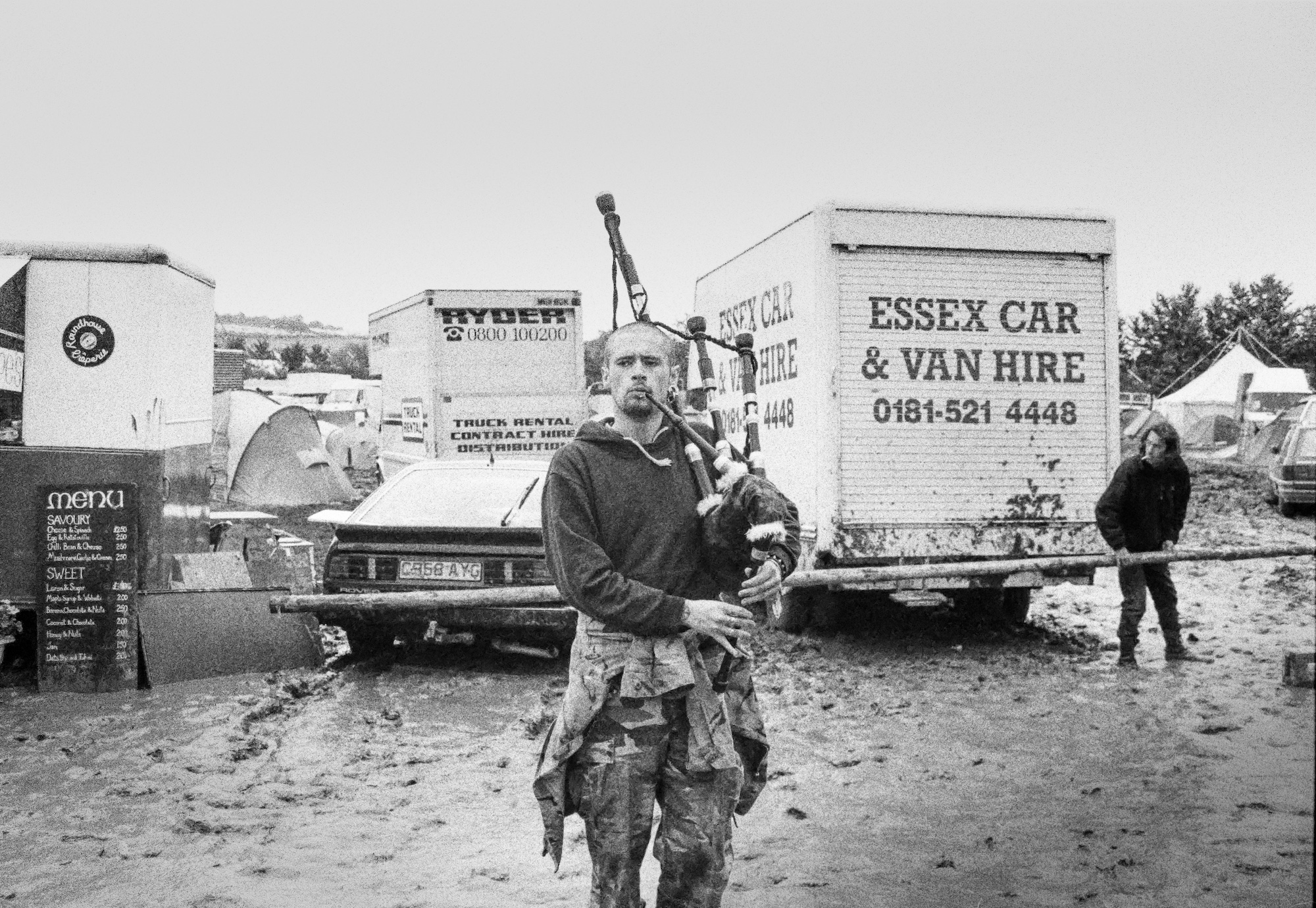 A man with a bagpipe stands in a muddy car park.