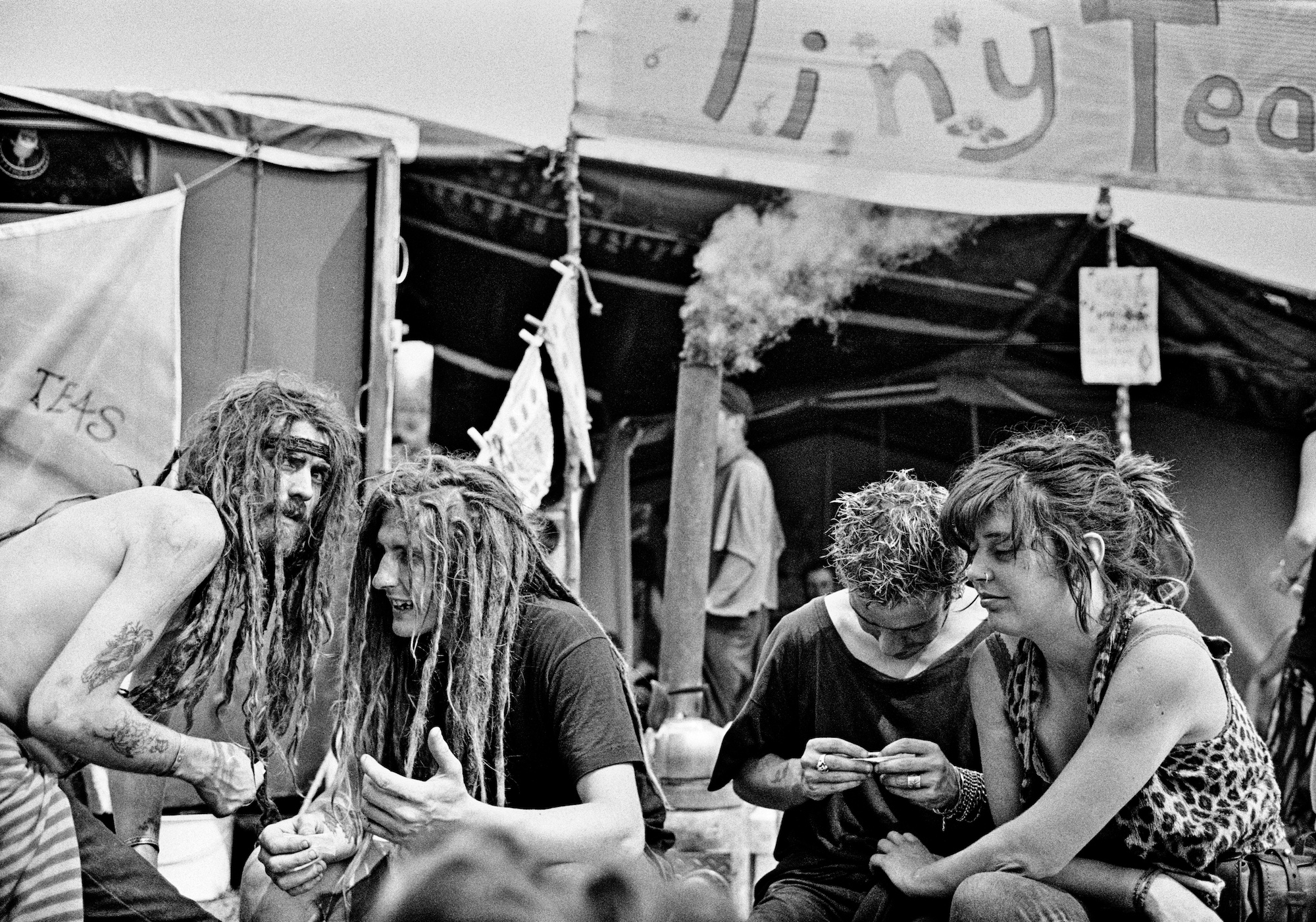 Two men with dreadlocks talk next to two other people rolling cigarettes.