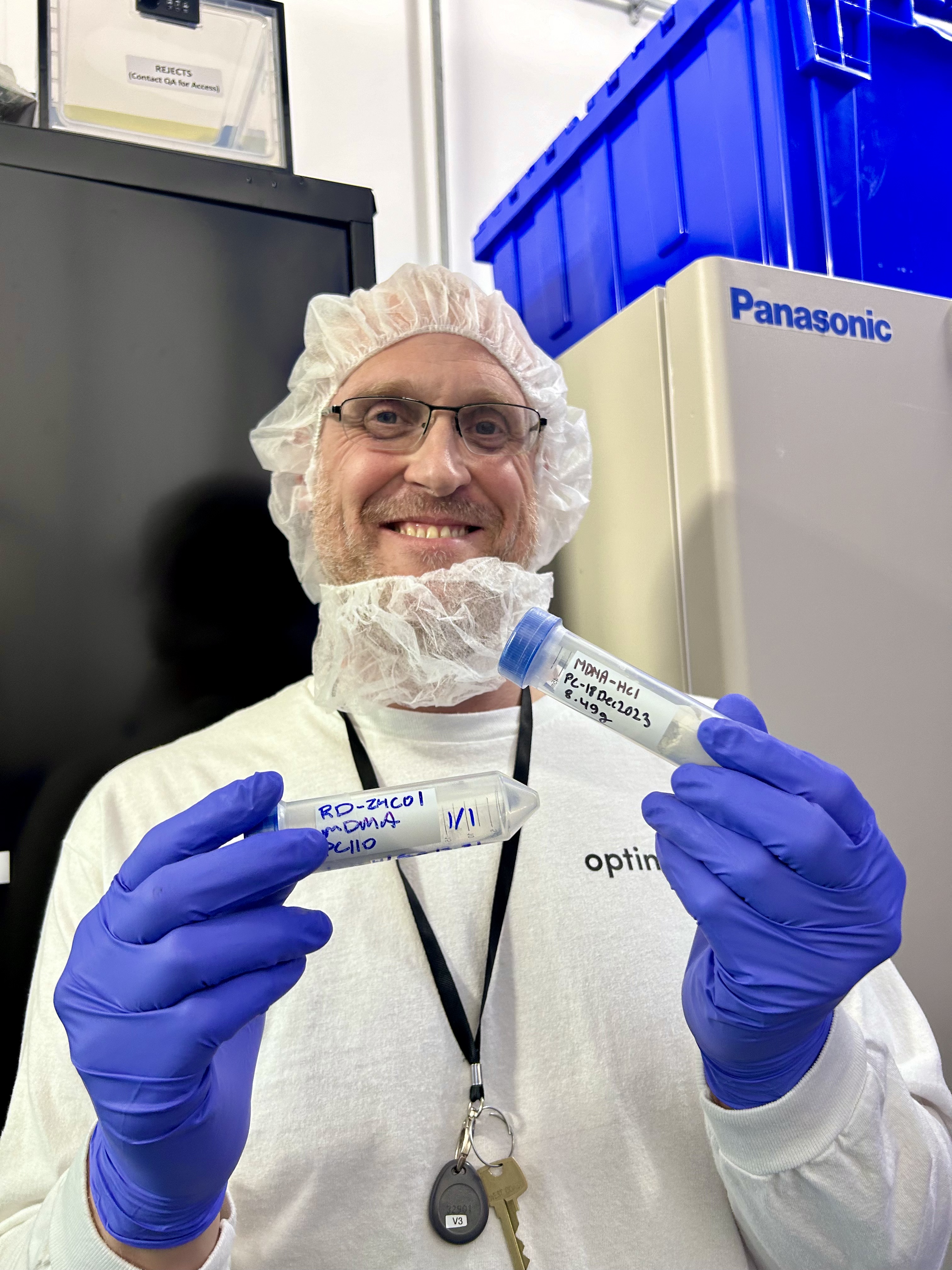 A scientist wearing protective gear holds two test tubes of MDMA