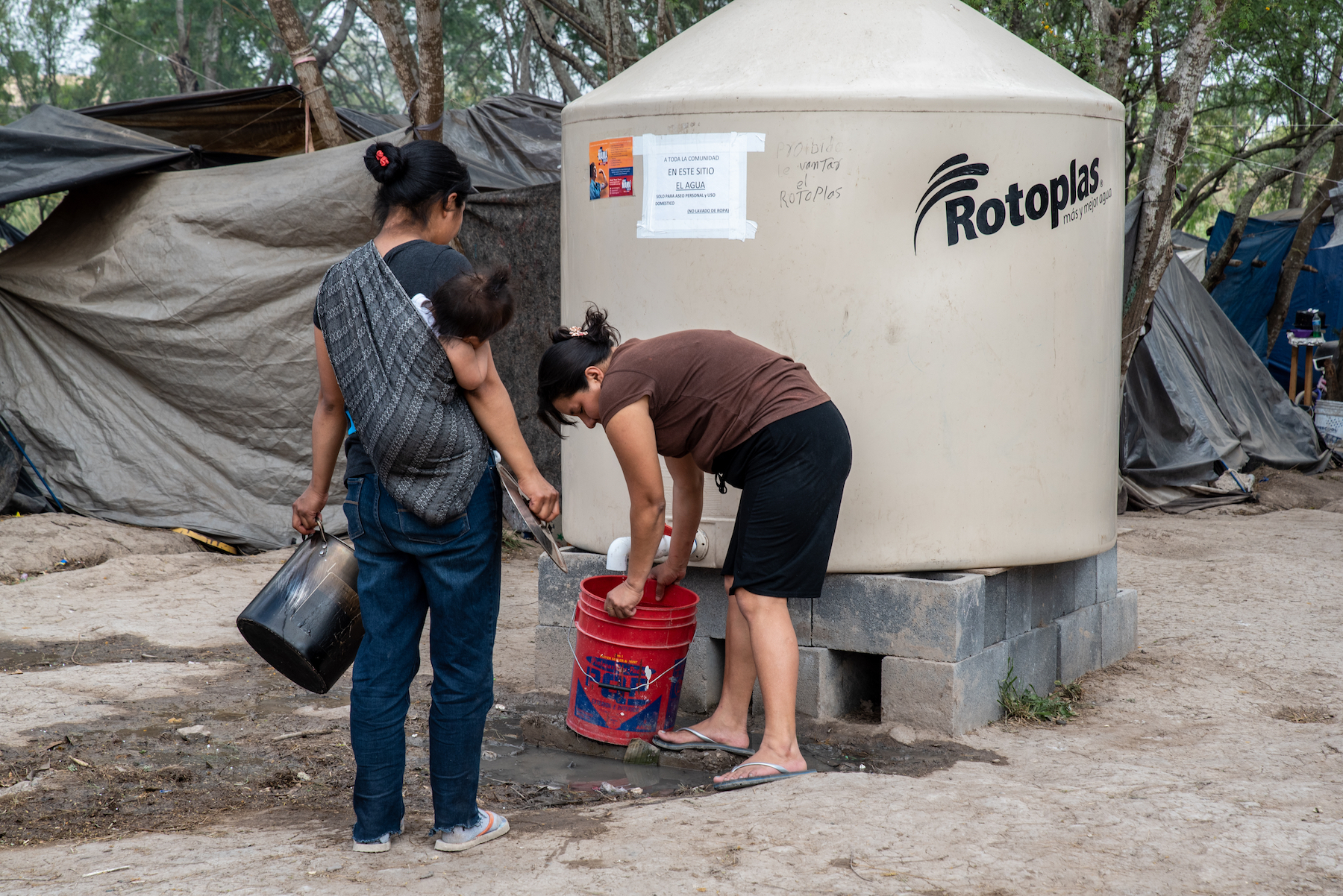 Women pour clean water into a bucket at the camp on March 2. Photo: Sergio Flores/VICE News.