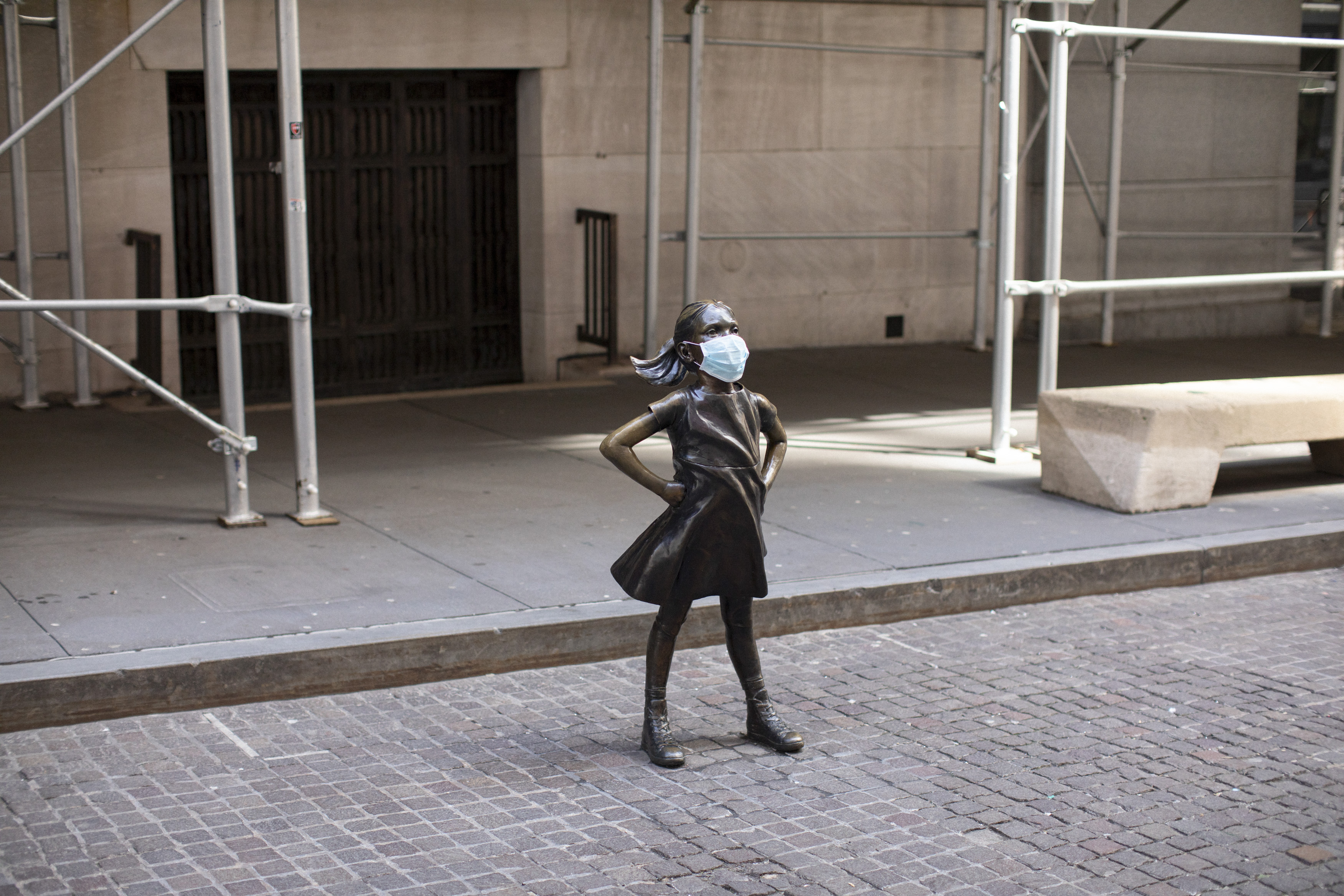 The Fearless Girl wears a face mask on an empty Broad Street outside the New York Stock Exchange.