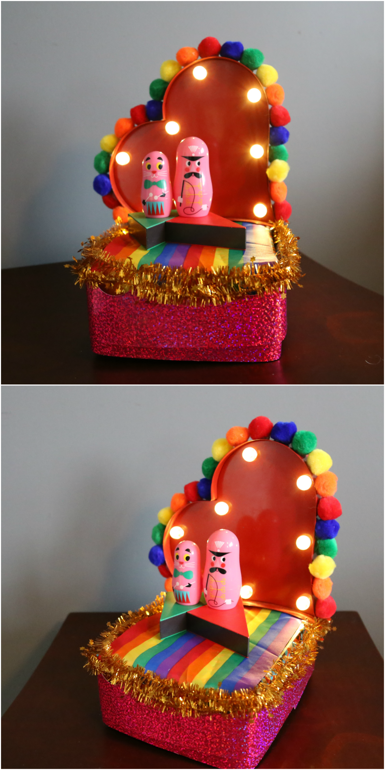 heart shaped box miniature pride parade float with lights, rainbow pompom trim, and two doll figured at the center