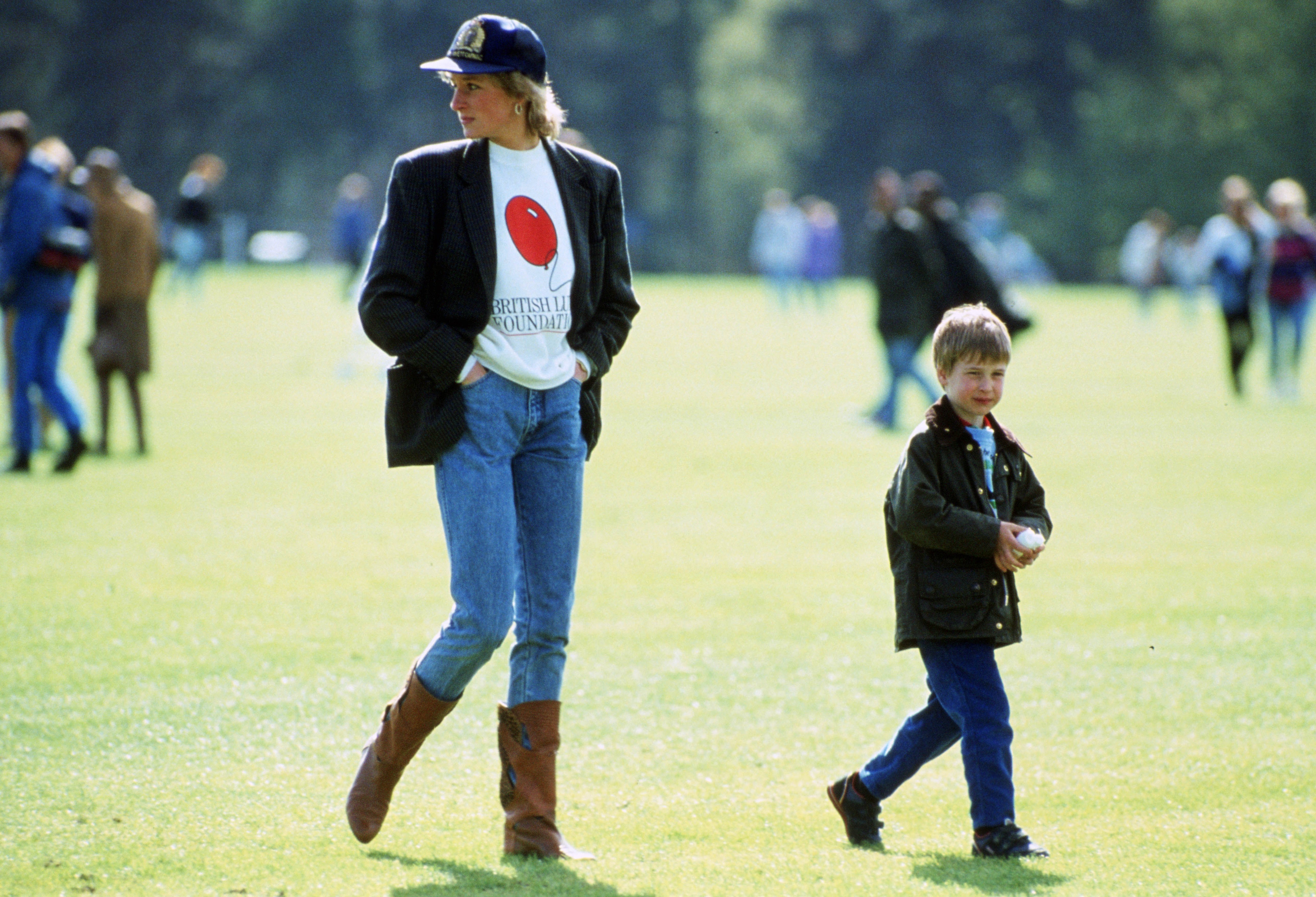 the princess and her son walk across a green, the former wearing brown cowboy boots, blue jeans and a british lung foundation sweatshirt under a black blazer